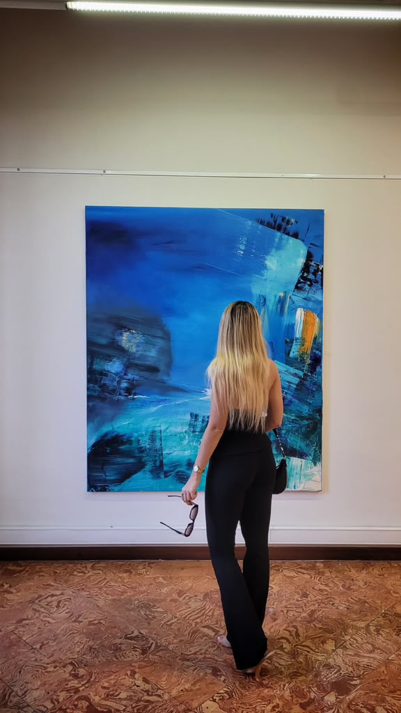 A visitor stands before a large blue abstract painting by Jeff Spees in a gallery.
